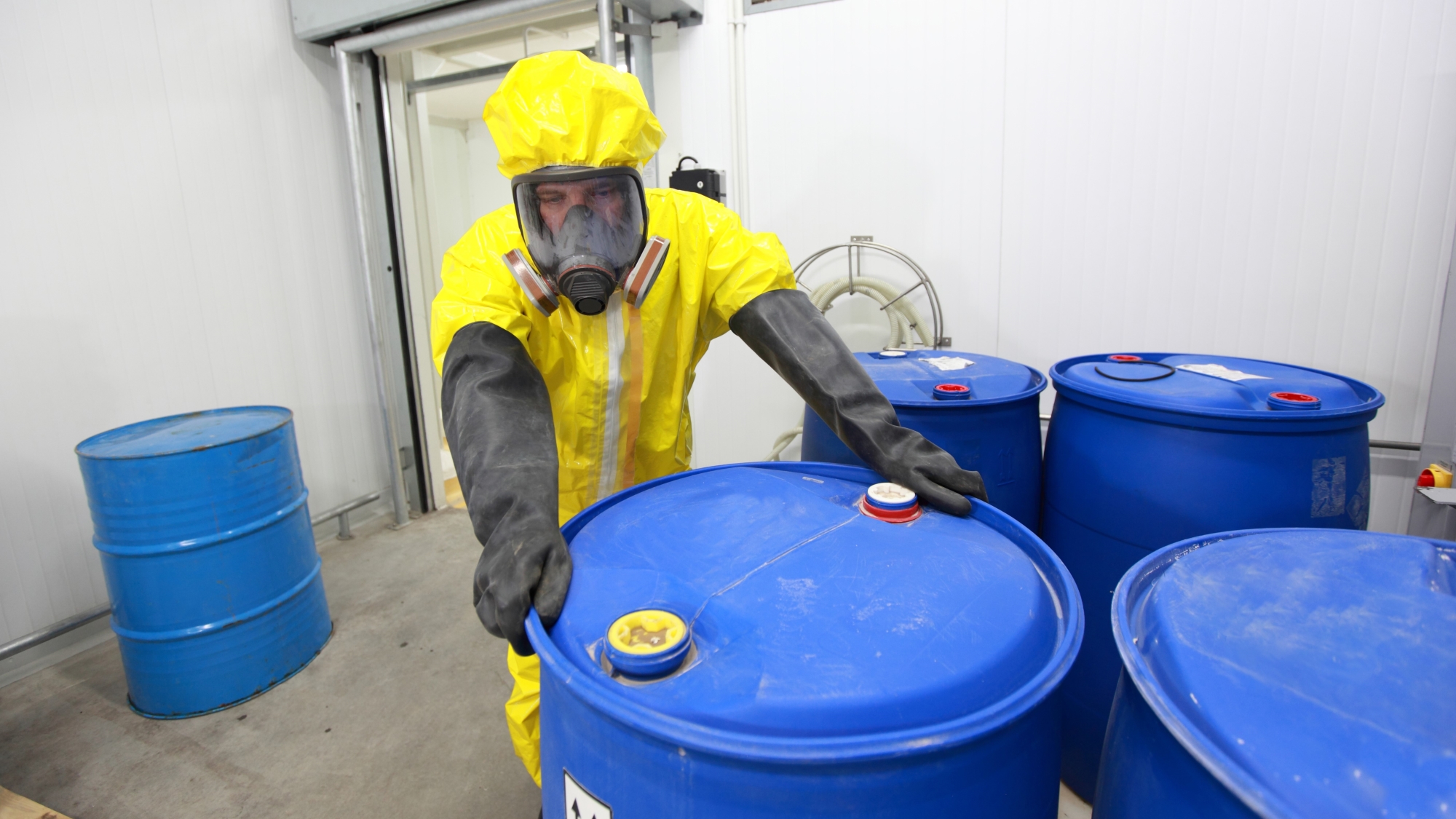 NEDT technician in full hazmat gear moving blue barrel into storage.