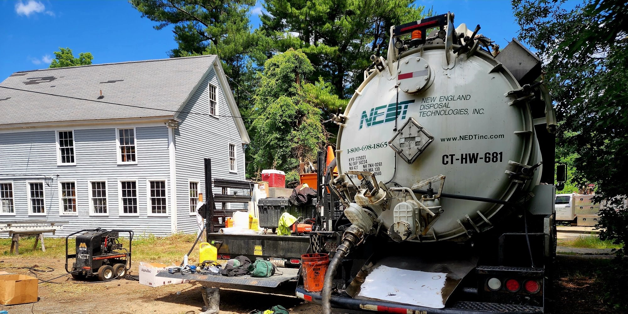 NEDT vacuum truck parked behind a residential building with hose deployed.