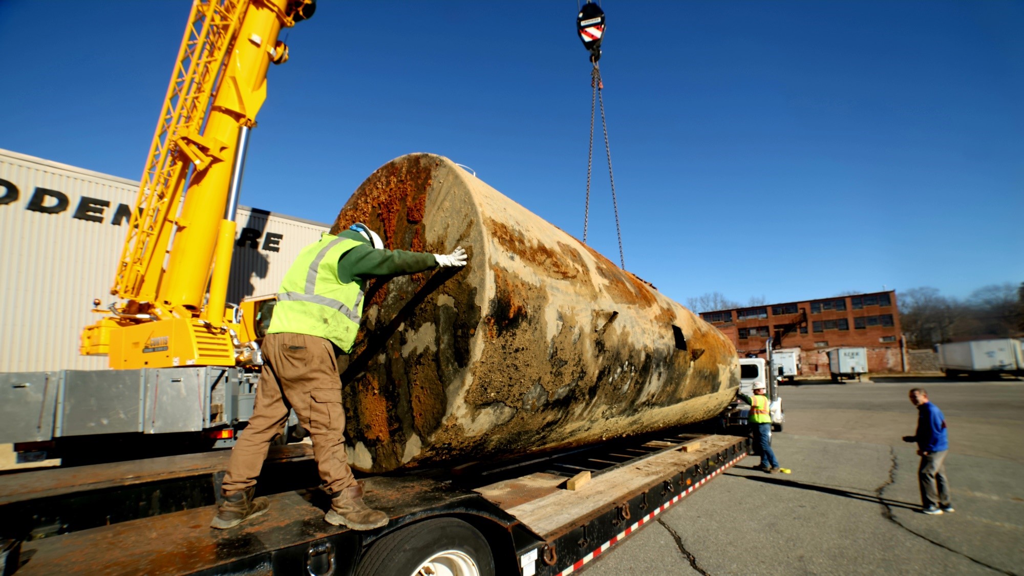 NEDT staff load a large underground storage tank onto a truck for disposal.